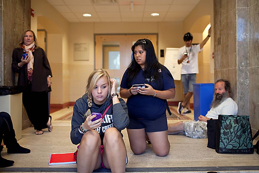 Students Paige Raiczyk, front left, and Veronica Rivera, front right and other University of Texas students and faculty hold their phones for updated text messages inside Benedict Hall on campus in Austin early Tuesday morning Sept. 28, 2010 after a shooting on campus. A gunman opened fire Tuesday inside a University of Texas campus library then fatally shot himself, and police are searching for a possible second suspect, university police said. (AP Photo/The Daily Texan, Tamir Kalifa)