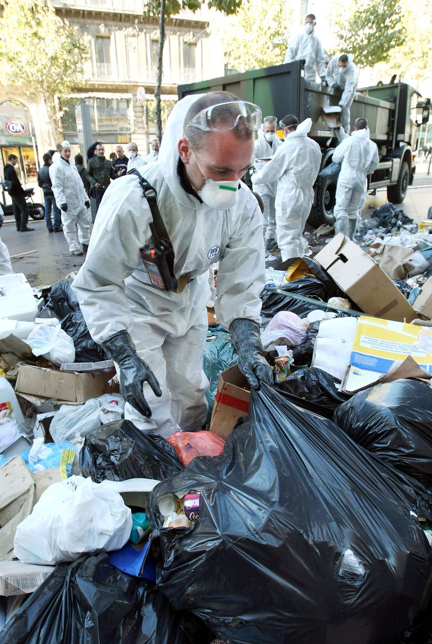 Civil security soldiers (left) collect garbage in central Marseille on Wednesday. The garbage collectors are on strike for nine days to protest against Mr. Sarkozy's plan to raise the retirement age to 62. (Associated Press)