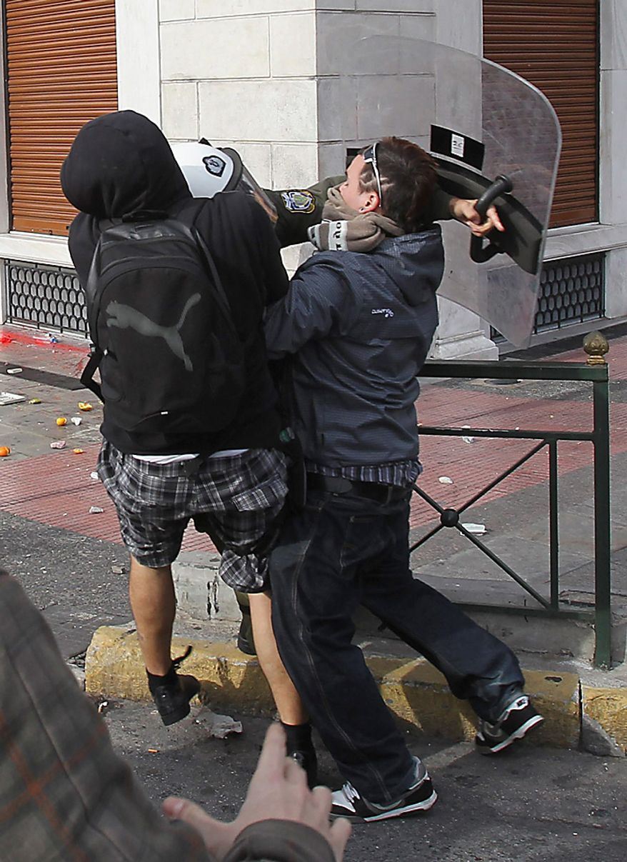 A youth with a bag attacks a riot police officer as another protester tries to restrain him during a rally in Athens on Monday, Dec. 6, 2010. Youths hurled rocks and oranges at a government building in central Athens during a student protest to mark two years since the fatal police shooting of a teenage boy that sparked Greece's worst riots in decades. Police closed roads and deployed several thousand officers around the city but maintained a minimal presence at the site where some 1,500 students gathered outside Athens University's main buildings. (AP Photo/Thanassis Stavrakis)
