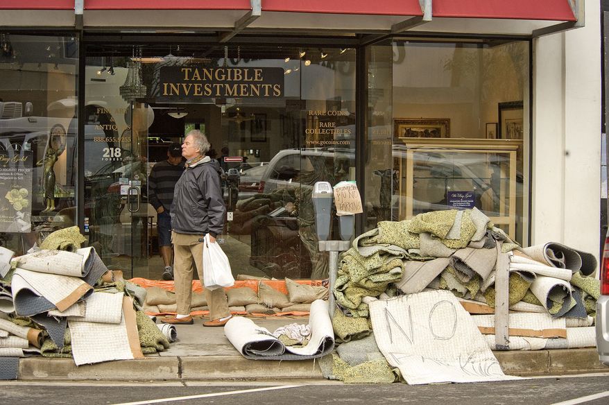 A passer-by walks past water-damaged carpet outside a business on Forest Avenue as Laguna Beach, Calif., cleans up and businesses open downtown on Thursday morning, Dec 23, 2010. (AP Photo/Orange County Register, Ken Steinhardt)