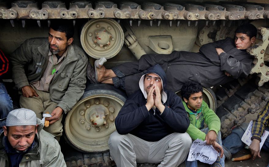 Anti-government protesters squat on the tracks of Egyptian army tanks Sunday to prevent them from moving near Tahrir Square in Cairo. (Associated Press)