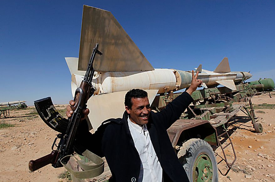 A Libyan popular defence committee, holds his AK-47 as he flashes V sign in front an anti-aircraft missile at an abandoned Libyan military base near Tobruk, Libya, on Wednesday, Feb.23, 2011. Heavy gunfire broke out in Tripoli as forces loyal to Moammar Gadhafi tightened their grip on the Libyan capital while anti-government protesters claimed control of many cities elsewhere and top government officials and diplomats turn against the longtime leader. (AP Photo/Hussein Malla)