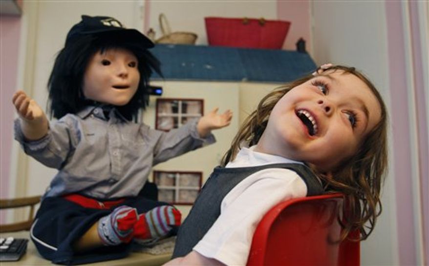 In this Monday, Feb. 28, 2011 photo, Ronnie Arloff smiles as he reacts to 'Kaspar' the robot as he takes part in research project, in Hatfield, England. Autistic children play with the robot for up to 10 minutes alongside a scientist who controls the robot with a remote control. The robot, named Kaspar, is programmed to do things like smile, frown, laugh, blink and wave his arms. He has shaggy black hair, a baseball cap, a few wires protruding from his neck, and striped red socks. He was built by scientists at the University of Hertfordshire at a cost of about 1,300 pounds ($2,118). (AP Photo/Alastair Grant)
