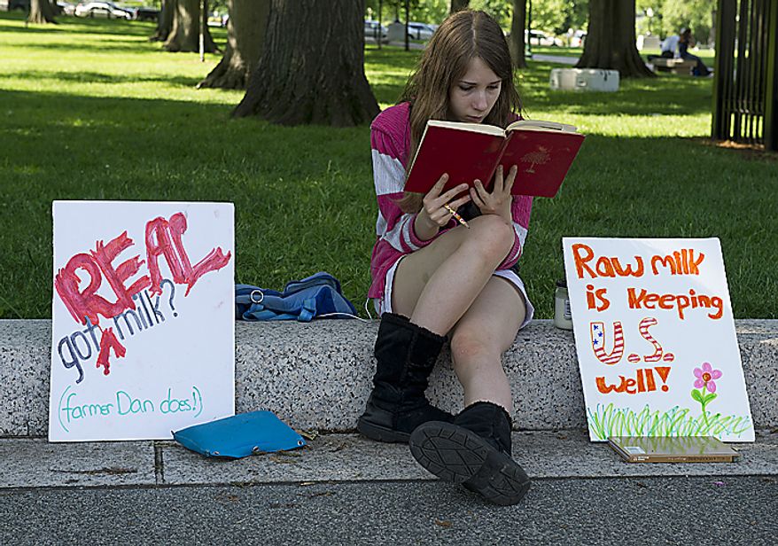 Fourteen-year-old Audrey Sarwer of Annapolis, Md., reads a book while sitting next to signs about raw milk at the Grassfed on the Hill rally at Upper Senate Park in Washington, D.C., on Monday, May 16, 2011. Her family gets fresh milk from Pennsylvania Amish dairy farmer Dan Allgyer, who was the subject of an FDA sting operation. The rally included samples of fresh milk, and Morgan the cow was also milked on site. (Barbara L. Salisbury/The Washington Times)
