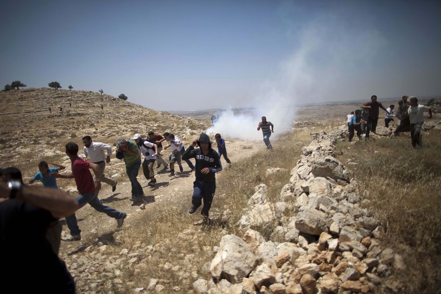 **FILE** Palestinians run from tear gas fired by Israeli soldiers during a demonstration against the expansion of nearby settlements at the West Bank village of Dier Qadis, near Ramallah, on June 15, 2011. (Associated Press)