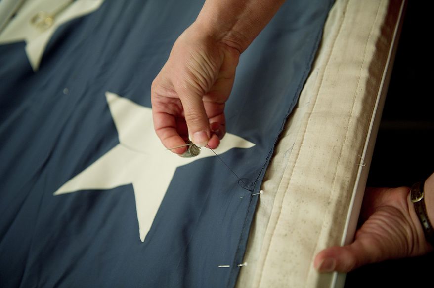 SPECIAL STITCHES: A woman stitches some of the blue fabric of the National 9/11 Flag during a ceremony to honor the victims. The flag was flying just south of the World Trade Center on Sept. 11, 2001. (Barbara L. Salisbury/The Washington Times)