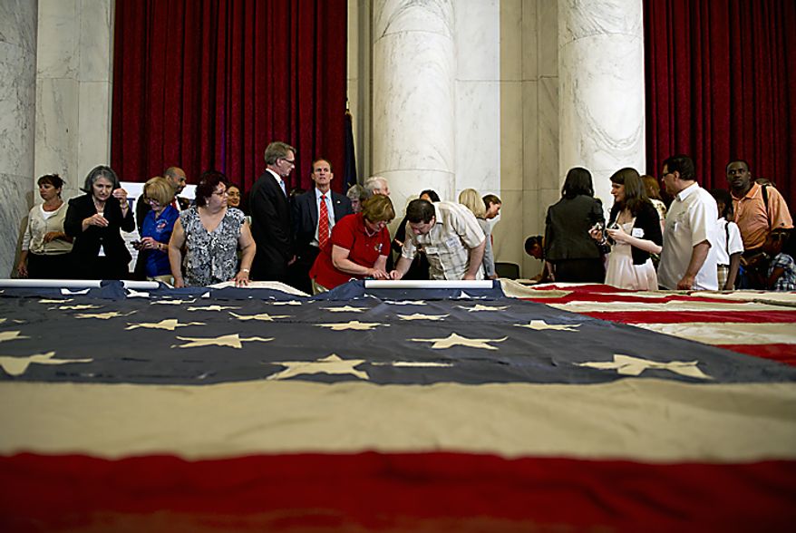 People line up to stitch the official 9/11 National flag during a stitching ceremony Thursday, July 14, 2011 at the Russell Senate Office Building in Washington, D.C. This flag, which was flying just south of the World Trade Center on Sept. 11, 2001, is making its way around the country and is being stitched back together by Americans, many of whom have suffered their own tragedies. Where pieces of the original flag are missing, people are adding their own pieces, including a piece of the flag that was laid under Pres. Abraham Lincoln after he had been shot. (Barbara L. Salisbury/The Washington Times)