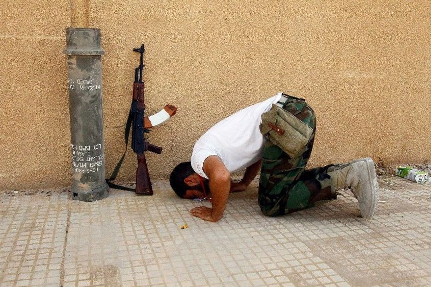 ASSOCIATED PRESS
MOMENT OF PEACE: A Libyan rebel prays Sunday outside an complex where rockets and shells were found. Internet postings by jihadists among the rebels reveal plotting to create an Islamic state.