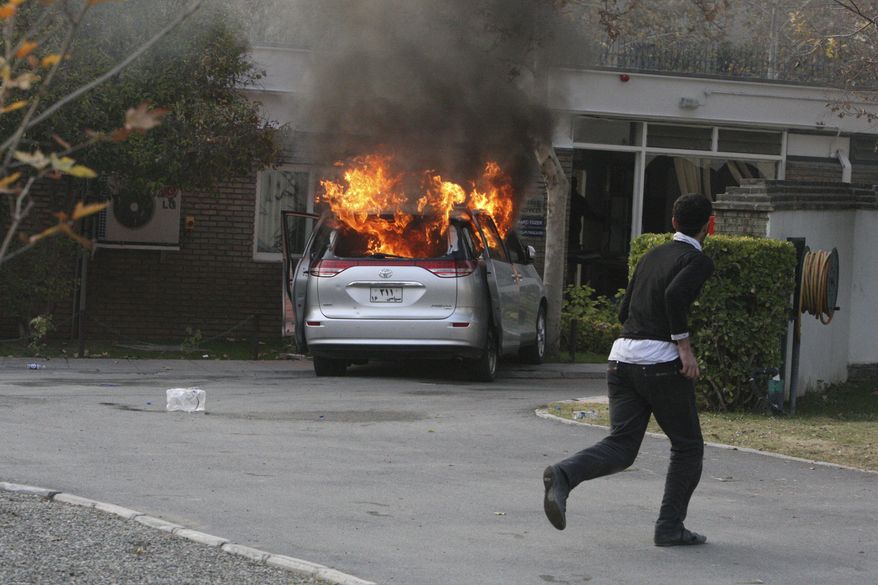 A hard-line Iranian protester runs inside the British Embassy in Tehran as a diplomatic vehicle is set on fire by demonstrators who stormed the embassy compound on Tuesday, Nov. 29, 2011. (AP Photo/Vahid Salemi)