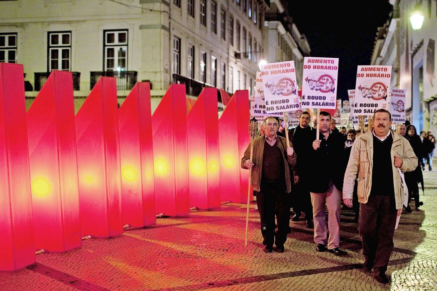 Demonstrators march past Christmas decorations in downtown Lisbon on Wednesday on their way to the finance ministry. They are protesting the government's proposal to increase the hours of work in a week. Portugal needed a $103 billion bailout earlier this year as its high debt load pushed it close to bankruptcy. The government is enacting an austerity program of pay cuts and tax hikes. The posters say "Increase in the work hours is robbing in the salary." (Associated Press)