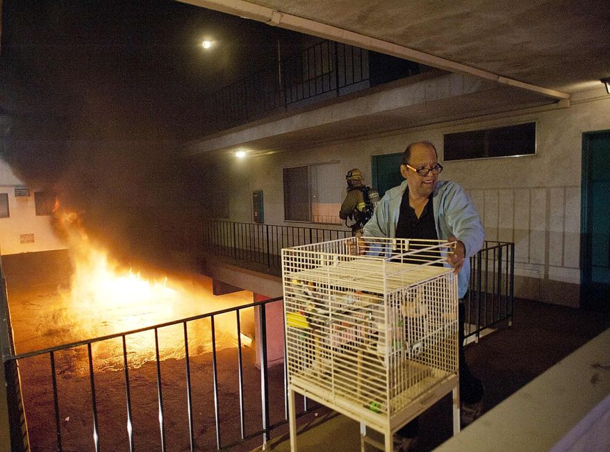 Los Angeles Fire Department firefighters assist a man out of his apartment along with a cage of birds as multiple cars burn in a carport in the Sun Valley neighborhood of Los Angeles on Saturday, Dec. 31, 2011. (AP Photo/Dan Steinberg)