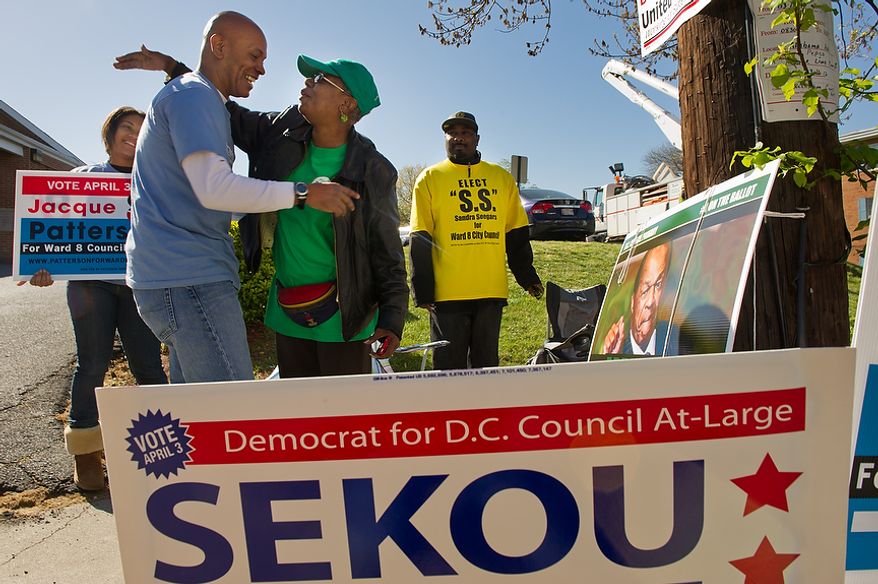 Posters for Ward 8 D.C. Council candidates surround former Ward 8 Democratic Party head Jacque Patterson (second from left), who is running for a council seat from the ward, as he hugs Kathy Arnold, a supporter of incumbent council member Marion Barry, also a Democrat, outside Precinct 116 at the New Image Baptist Church on Alabama Avenue Southeast in Washington on Tuesday, April 3, 2012. Also pictured is Jasmine Westbrook (left), a Howard University sophomore volunteering with Mr. Patterson, and Craig Leak (right), a volunteer with council candidate Sandra Seegers. (Andrew Harnik/The Washington Times)