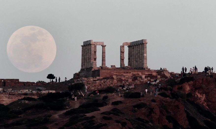 The "supermoon" appears behind the Temple of Poseidon on Cape Sounion, southeast of Athens, while tourists watch on Saturday, May 5, 2012. (AP Photo/Dimitri Messinis)