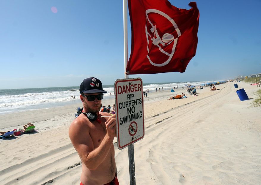 Evan Anderson, Carolina Beach Ocean Rescue squad leader, places a sign in the sand closing the beach to swimming on Saturday, May 26, 2012, at Carolina Beach, N.C., because of strong rip currents. (AP Photo/The Star-News, Matt Born)