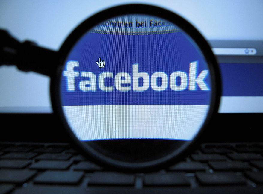 ** FILE ** A magnifying glass is posed over a monitor displaying a Facebook page in Munich on Oct. 10, 2011. (Associated Press)
