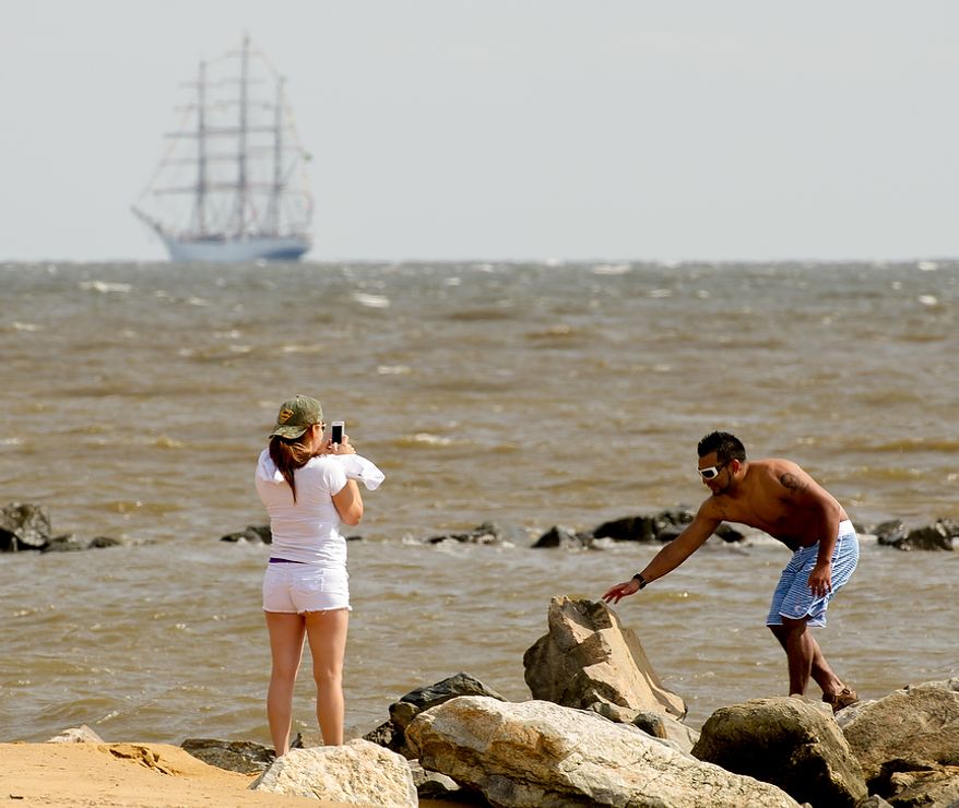 Caroline Amaya (left), of Gaithersburg, Md., takes a photograph of her husband, Sergio, at Sandy Point State Park in Annapolis, Md., on June 13, 2012, as tall ships pass under the Chesapeake Bay Bridge en route to the Inner Harbor in Baltimore for a bicentennial commemoration of the War of 1812. The week-long "Star-Spangled Sailabration" includes free tours of the ships, waterside festivities, an air show featuring the Blue Angels and the world premiere of "Overture for 2012," composed by Philip Glass. (Andrew Harnik/The Washington Times)