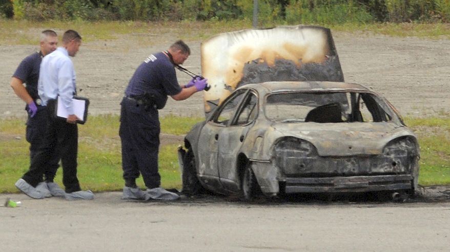 Police investigate a vehicle that burned before dawn on Aug. 13, 2012, off Target Industrial Circle in Bangor, Maine. After the fire was extinguished, three bodies were found inside the parked car. (Associated Press/Bangor Daily News, Gabor Degre)