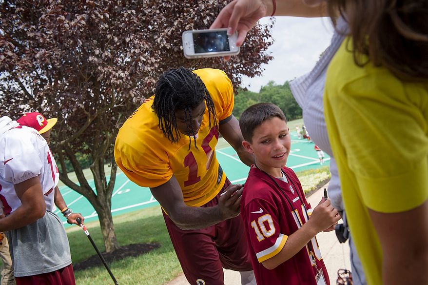 Redskins quarterback Robert Griffin III signs the jersey for an unidentified young man following Redskins training camp at Redskins Park in Ashburn, Va., Tuesday, August 14, 2012. This is the last day that fans will be able to watch their team practice in this area. Next year the Redskins will move their practice facility to the Richmond, Va., area. (Rod Lamkey Jr./The Washington Times)