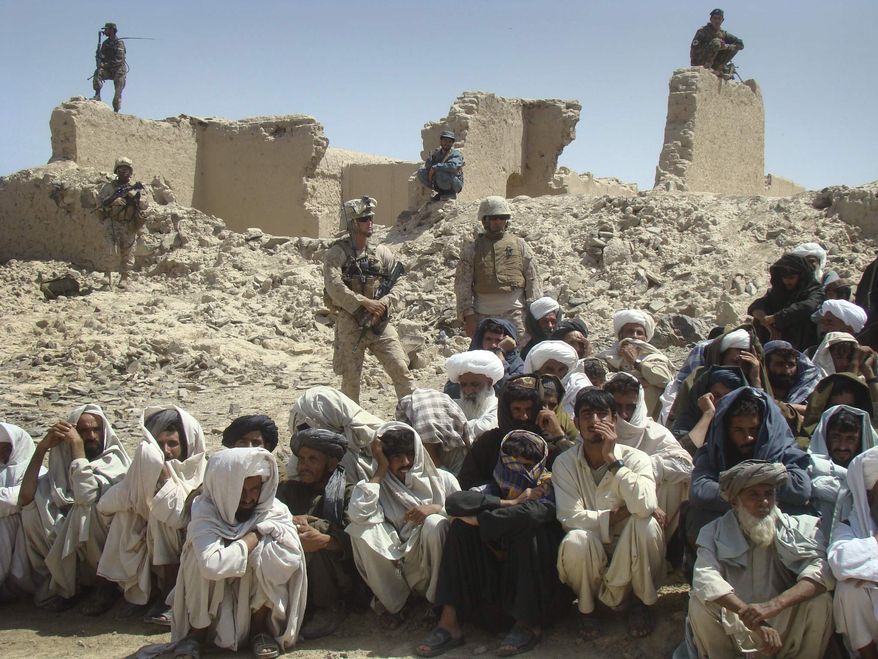 In this Saturday, Aug. 27, 2011, photo, Afghan men listen to speeches, as Afghan and U.S. soldiers stand guard, background, in Washer district, Helmand province, south of Kabul, Afghanistan. (AP Photo/Abdul Khaleq)