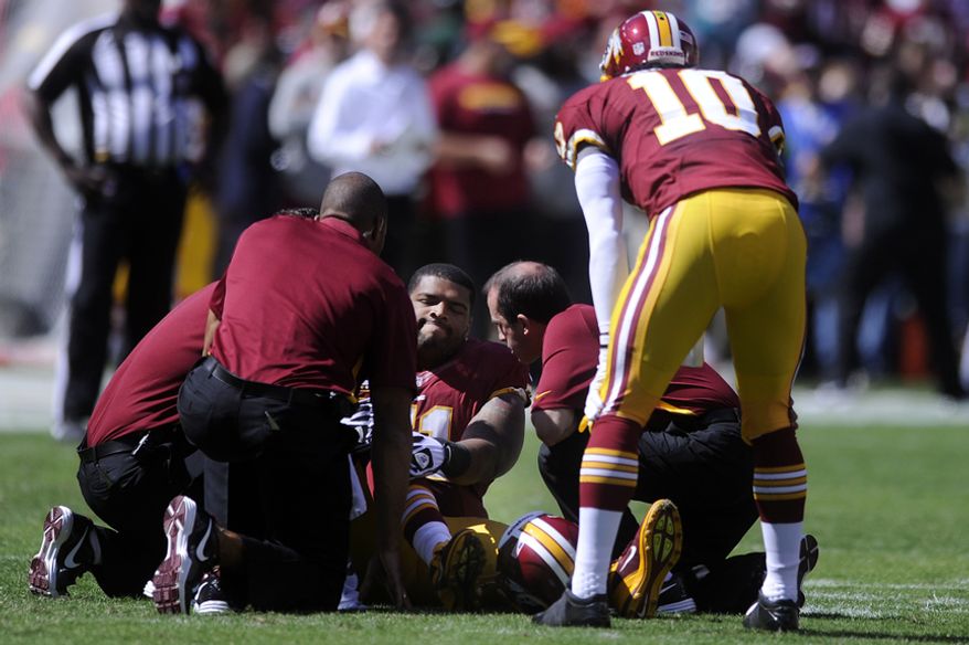 Washington Redskins tackle Trent Williams (71) sits injured on the field as quarterback Robert Griffin III (10) looks on at FedEx Field, Landover, Md., Sep. 23, 2012. (Preston Keres/Special to The Washington Times)