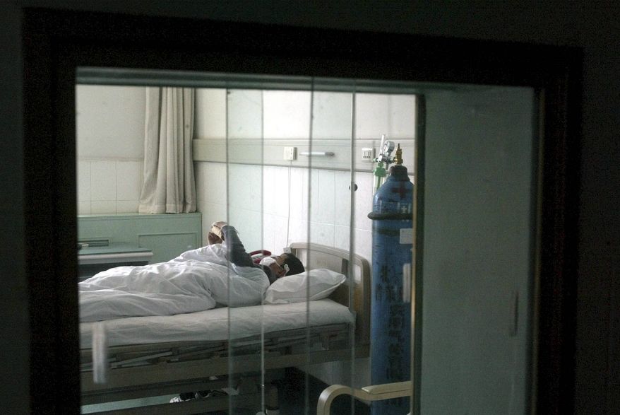 **FILE** A SARS patient receives treatment behind double-layer glass windows and strict quarantine measures at the Beijing Ditan Hospital in Beijing on April 13, 2003. (Associated Press)