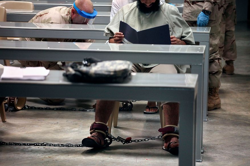 In this photo, made through one way glass, reviewed by the U.S. military, a shackled Guantanamo detainee reads his materials as he attends a class in "Life Skills," as guards in the background shackle another detainee to the floor after bringing him to the class, inside Camp 6 high-security detention facility at Guantanamo Bay U.S. Naval Base, Cuba, Tuesday, March 30, 2010. The Obama Administration is pushing to close the Guantanamo detention facility, by transferring, prosecuting, or releasing the remaining detainees. (AP Photo/Brennan Linsley)
