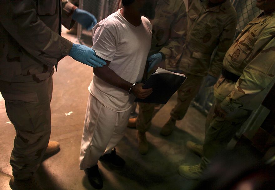 In this March 30, 2010 photo made through one way glass and reviewed by the U.S. military, a Guantanamo detainee carries a workbook while escorted by guards after attending Life Skills class in Camp 6 high-security detention facility on Guantanamo Bay U.S. Naval Base in Cuba. The Obama administration is pushing to close the Guantanamo detention facility by transferring, prosecuting or releasing the remaining detainees. (AP Photo/Brennan Linsley)