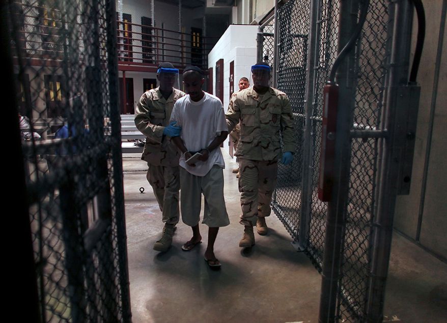 In this March 30, 2010 photo, made through one way glass, reviewed by the U.S. military, a Guantanamo detainee carries a workbook as he is escorted by guards after the detainee attended a class in "Life Skills," inside Camp 6 high-security detention facility at Guantanamo Bay U.S. Naval Base, Cuba. The Obama Administration is pushing to close the Guantanamo detention facility, by transferring, prosecuting, or releasing the remaining detainees. (AP Photo/Brennan Linsley)