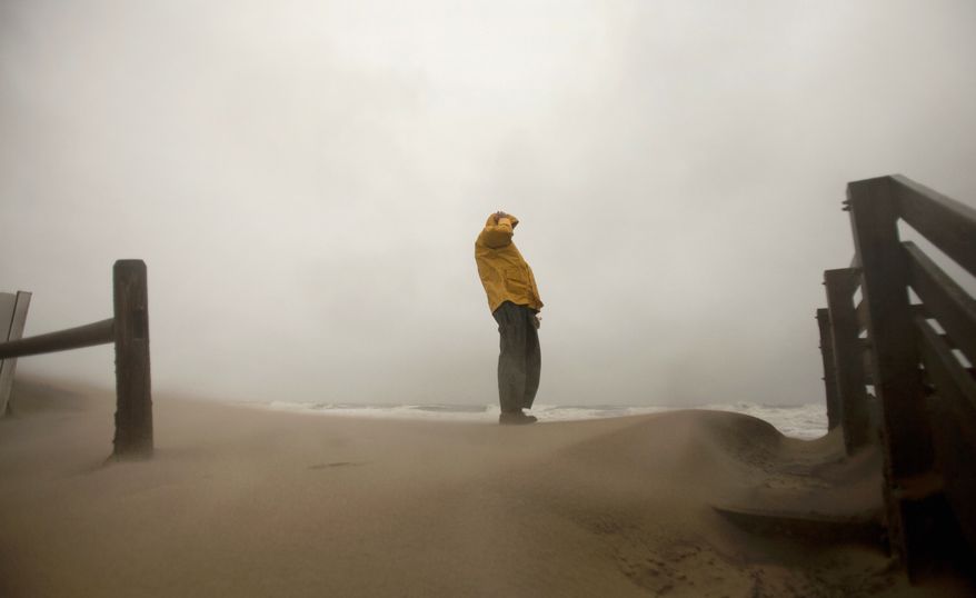 Matt Francis of Virginia Beach holds on to his hat as the wind-driven sand and rain from Hurricane Sandy blow across the beaches of Sandbridge in Virginia Beach on Sunday, Oct. 28, 2012. (L. Todd Spencer/The Virginian-Pilot)