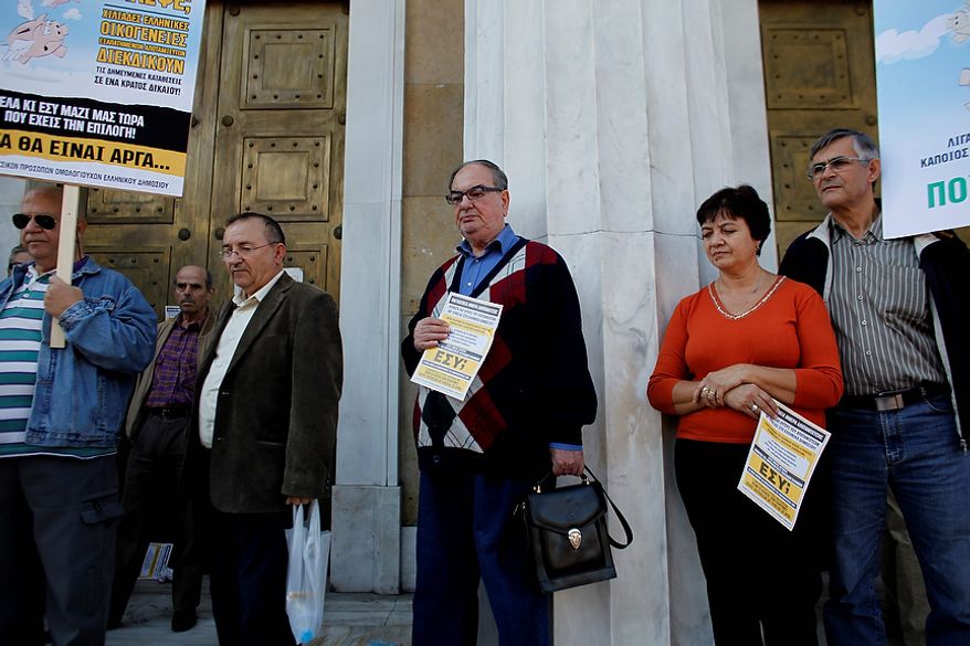 Greek bond holders stand at the entrance of Greece's central bank during a protest, in Athens Wednesday, Oct. 31 2012. Greece's two main labor unions covering civil servants and the private sector have called a 48-hour strike to protest austerity measures due to be voted on next week. The strike call came as the finance minister submitted an amended 2013 budget that raised the country's debt and deficit forecasts for next year. (AP Photo/Kostas Tsironis)