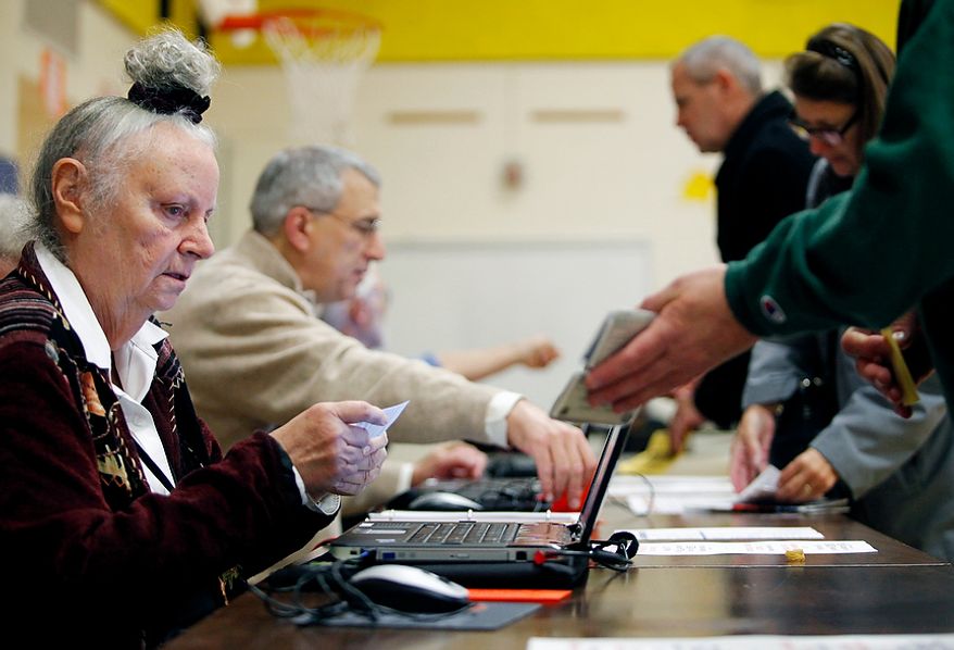 Election officers check voters' identification at Washington Mill Elementary School in Alexandria, Va., on Nov. 6, 2012. (Eva Russo/Special to The Washington Times)