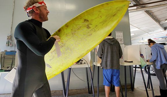 After voting, Mike Weigart, 30, carries his ballot and his surfboard to the ballot box at the polling place at the Venice Beach lifeguard headquarters in Los Angeles Tuesday, Nov. 6, 2012. Weigart said "It's awesome the polling place is where I surf." (AP Photo/Reed Saxon)