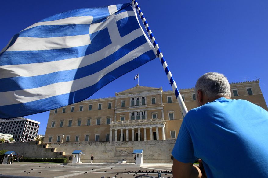 ** FILE ** A protester holding a Greek flag looks at the Greek Parliament in Athens on Tuesday, Nov. 6, 2012. Greece's unions are holding their third general strike in six weeks to press dissenters in the country's troubled coalition government not to back a major new austerity program that will doom Greeks to further hardship in a sixth year of recession. (AP Photo/Nikolas Giakoumidis)