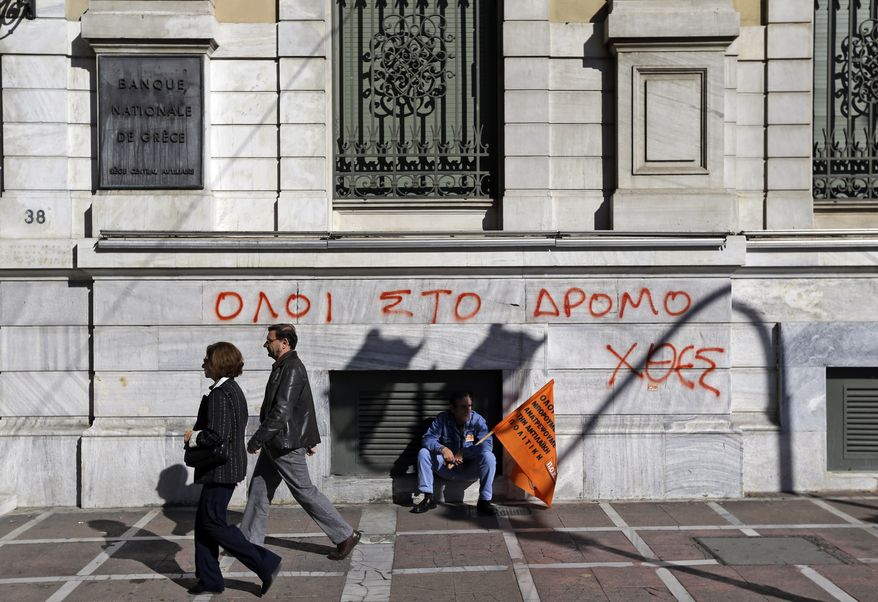 A municipal worker participating in a anti-austerity rally sits Nov. 9, 2012, in central Athens in front of the National Bank of Greece building, underneath graffiti reading in Greek "All to the streets yesterday." (Associated Press)