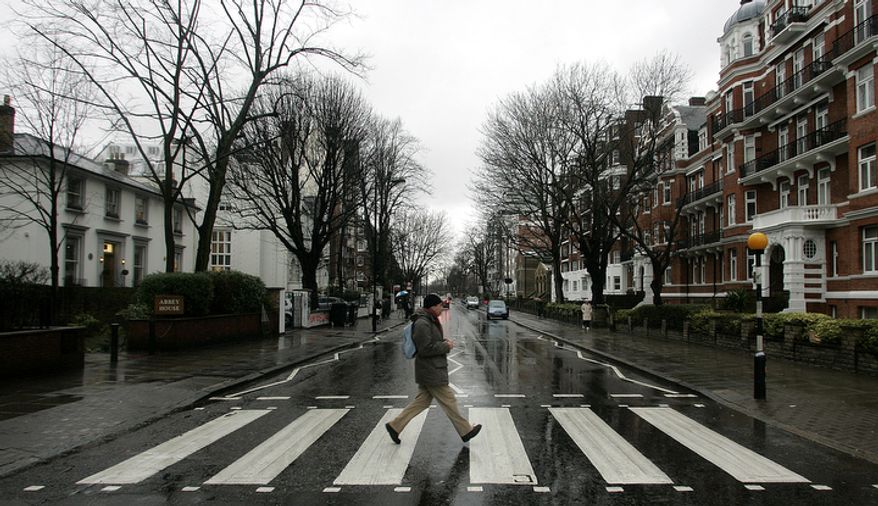 In this file photo dated Feb. 16, 2010, a man walks across the zebra crossing made famous from the album cover of The Beatles 'Abbey Road' in front of Abbey Road Studios, seen at left, in London. Feb. 16, 2010. Struggling music company EMI Group has shelved plans to sell Abbey Road, the London recording studio made famous by The Beatles. The company now says, Monday Feb. 22, 2010, it wants to keep the facility and is talking to "interested and appropriate third parties" about a revitalization project. (AP Photo/Akira Suemori, File)