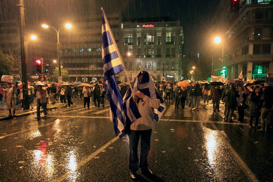 A protester takes cover from the rain after a protest near the parliament during clashes in Athens on Wednesday Nov. 7, 2012. (AP Photo Nikolas Giakoumidis)