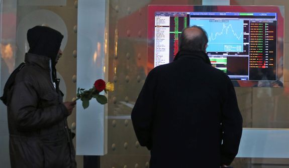 A man checks a monitor with stock exchange data as a flower seller approaches him in Milan, Italy, on Dec. 10, 2012. (Associated Press)