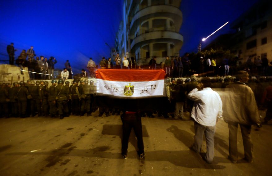 A protester holds the Egyptian national flag as army soldiers stand guard near the presidential palace in Cairo on Dec. 9, 2012. (Associated Press)