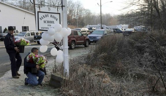 A couple of volunteer firefighters place flowers at a makeshift memorial at a sign for the Sandy Hook Elementary school, Saturday, Dec. 15, 2012, in Sandy Hook village of Newtown, Conn. (AP Photo/Mary Altaffer)