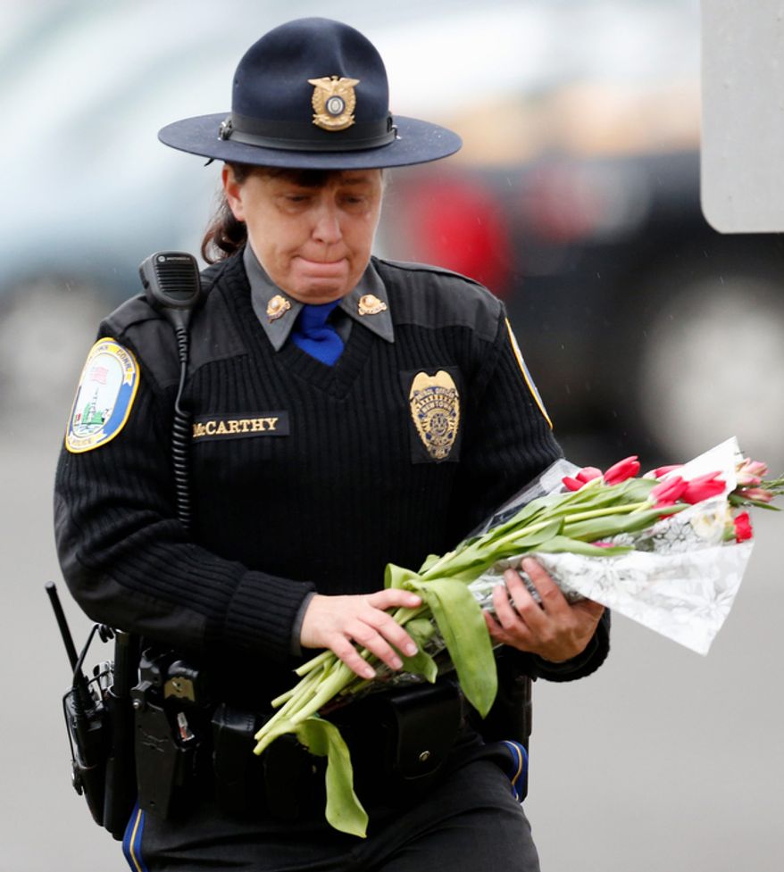 Newtown Police Officer Maryhelen McCarthy places flowers at a makeshift memorial outside St. Rose of Lima Roman Catholic Church, Sunday, Dec. 16, 2012, in Newtown, Conn. (AP Photo/Julio Cortez)