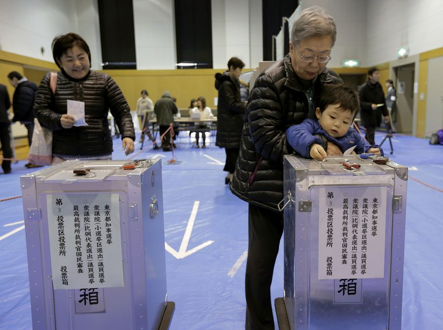 A boy slips his grandmother's vote into a ballot box at a polling station in Tokyo on Sunday, Dec. 16, 2012. (AP Photo/Itsuo Inouye)