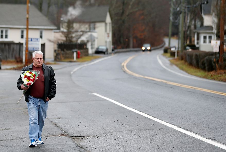 A man walks with flowers in the Sandy Hook village of Newtown, Conn., on Monday, Dec. 17, 2012, as the town mourns those killed in Friday's school shooting. (AP Photo/Julio Cortez)