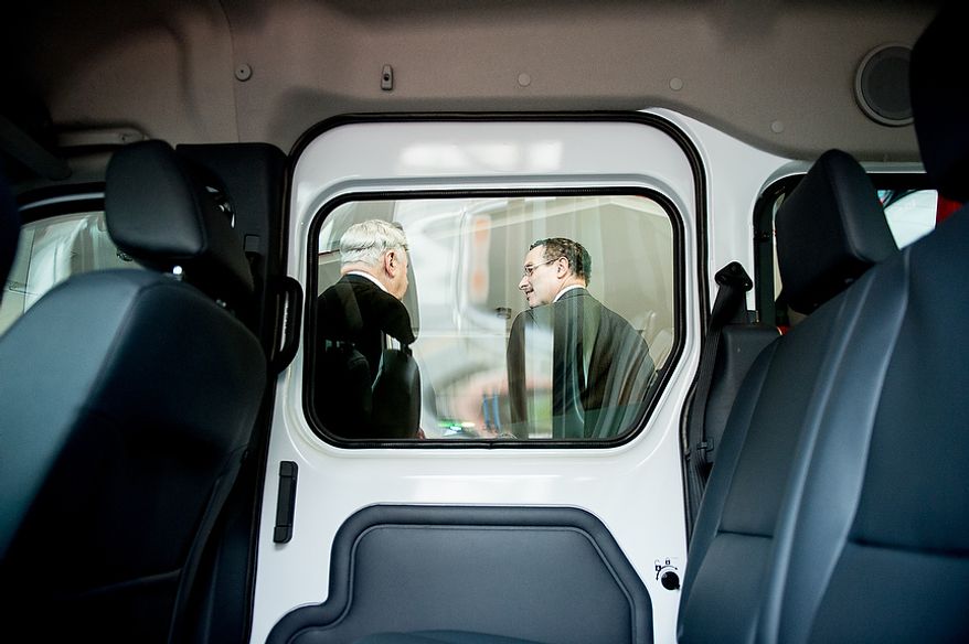 Washington Mayor Vincent C. Gray (right) and D.C. Taxicab Commission Chairman Ron M. Linton (left) are seen through the window of a model taxi cab as they display four of the proposed 10 uniform color designs for Washington's taxicab fleet at the Verizon Center in Washington's Chinatown neighborhood on Monday, Dec. 10, 2012. The city is asking residents to weigh in on which design they favor before officials decide which color scheme will become the uniform design for all cabs in the city. (Andrew Harnik/The Washington Times)