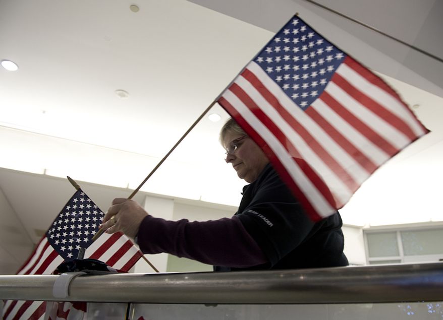 ** FILE ** Jan Feldman with Operation Welcome Home Maryland puts up American flags at the international arrivals area of BWI Thurgood Marshall Airport on Friday, Dec. 28, 2012, in preparation of welcoming a charter flight of military personnel back home. The welcome organization has greeted more than 800 flights and 180,000 troops since its inception in 2007. (Barbara L. Salisbury/The Washington Times)