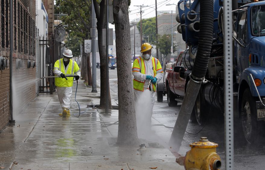 **FILE** Sanitation workers in a protective suits clean a street in the heart of the Skid Row district in downtown Los Angeles on June 20, 2012. The three-week cleanup that started this week will get rid of rats' nests, hypodermic needles, condoms, human excrement and other hazards. Weekly inspections will follow. A federal court injunction last year placed limits on the removal of unattended items, but doesn't prevent removal of items that pose health risks. (Associated Press)