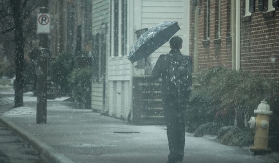 An Old Town resident uses his umbrella to shield his face from the snow in Alexandria, Va., Wednesday, March 6, 2013. (Andrew S. Geraci/The Washington Times)