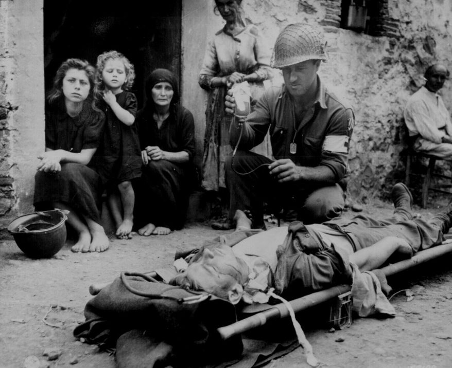 "Private Roy Humphrey is being given blood plasma by Pfc. Harvey White, after he was wounded by shrapnel, on 9 August 1943 in Sicily." (U.S. National Archives)