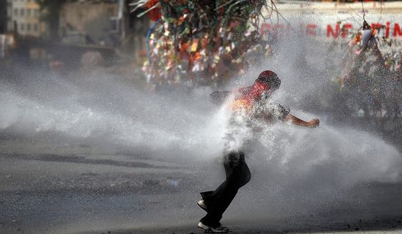 A protester tries to remain standing against the force of a police water cannon during clashes in Taksim Square in Istanbul on Tuesday, June 11, 2013. Hundreds of police in riot gear forced through barricades and pushed many of the protesters who had occupied the square for more than a week into a nearby park. (AP Photo/Kostas Tsironis)