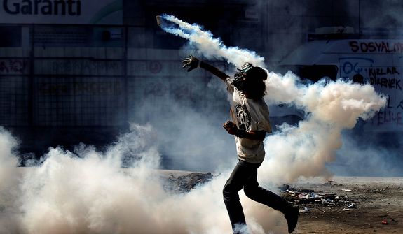A protester throws a tear gas canister back to police during clashes in Taksim Square in Istanbul on Tuesday, June 11, 2013. Hundreds of police in riot gear forced through barricades and pushed many of the protesters who had occupied the square for more than a week into a nearby park. (AP Photo/Kostas Tsironis)