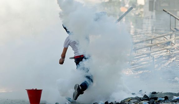 A protester throws back a tear gas canister toward riot police during clashes in Taksim Square in Istanbul on Tuesday, June 11, 2013. Hundreds of police in riot gear forced through barricades and pushed many of the protesters who had occupied the square for more than a week into a nearby park. (AP Photo/Vadim Ghirda)